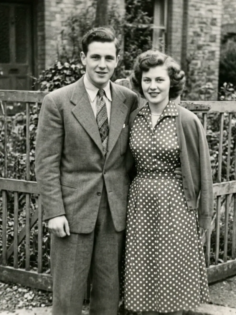 A young couple in a suit and polka dot dress at a garden gate, 1950s black-and-white photo